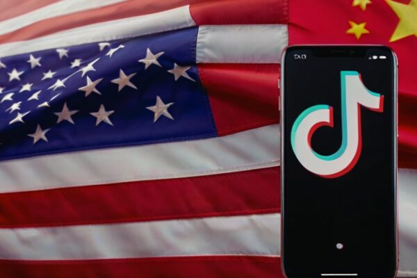 In den USA könnt ein mögliches TikTok Verbot kurz bevorstehen. Auf dem Foto sieht man im Vordergrund ein Handy, auf dessen Bildschirm das TikTok Logo zu sehen ist. Im Hintergrund sieht man die chinesische und die amerikanische Flagge.