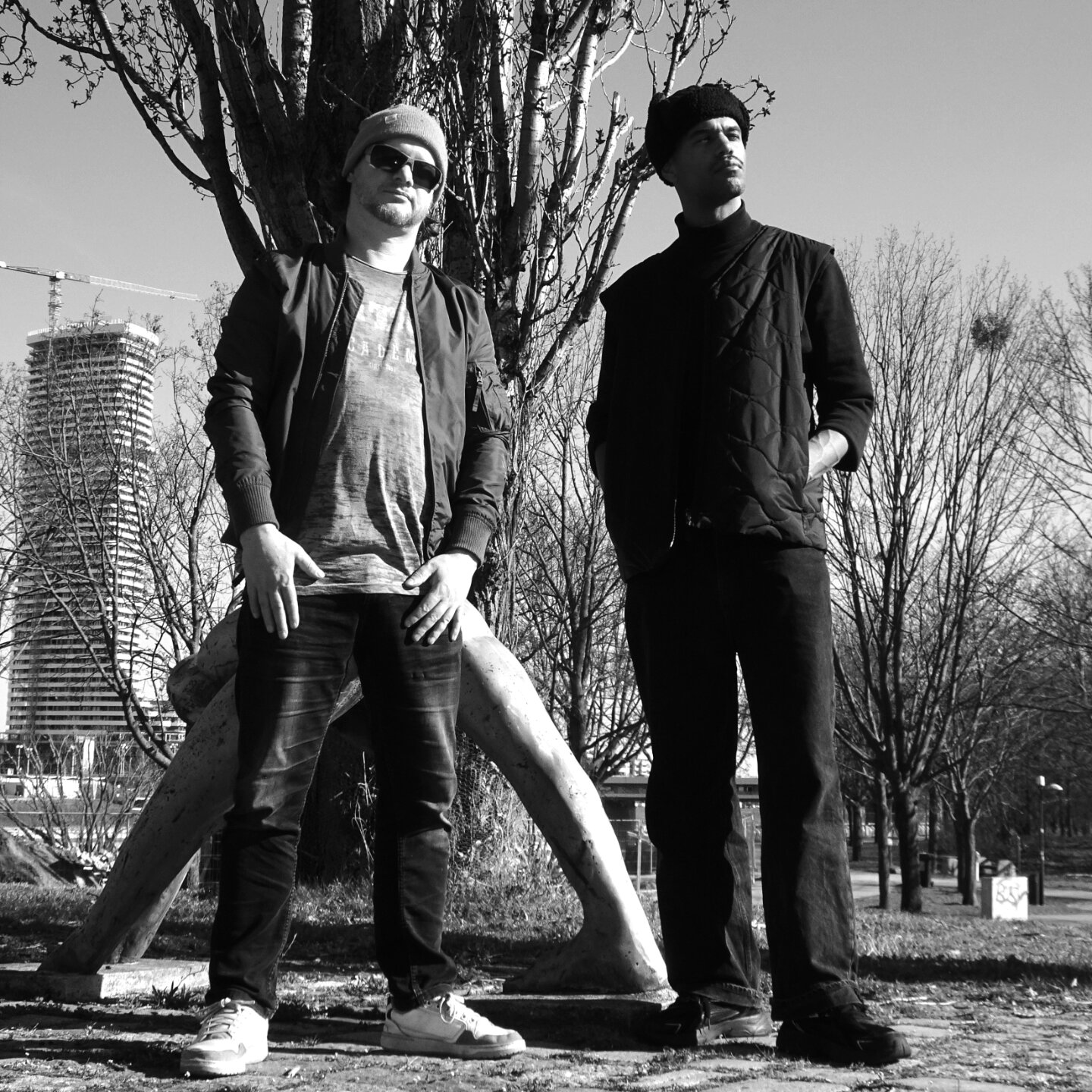 Ein schwarz-weißes Foto von Seha EKs & Hightauer. Die beiden Rapper stehen vor einem Baum. Hightauer steht zur Rechten und Seha Eks zur Linken. 