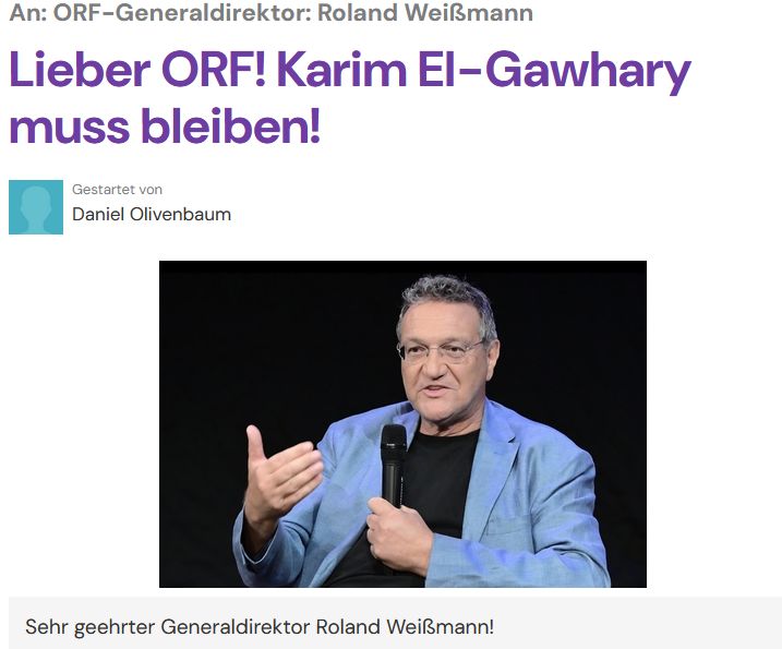 Auf dem Bild ist der ORF-Journalist Karim El-Gawhary zu sehen, wie er auf einer Bühne sitzt und in ein Handmikrofon spricht. Er trägt ein hellblaues Sakko über einem dunklen Shirt und gestikuliert mit der freien Hand, als würde er einen Punkt erläutern. Der Hintergrund ist dunkel gehalten, wodurch der Fokus klar auf seiner Person und seinem konzentrierten, erklärenden Ausdruck liegt.